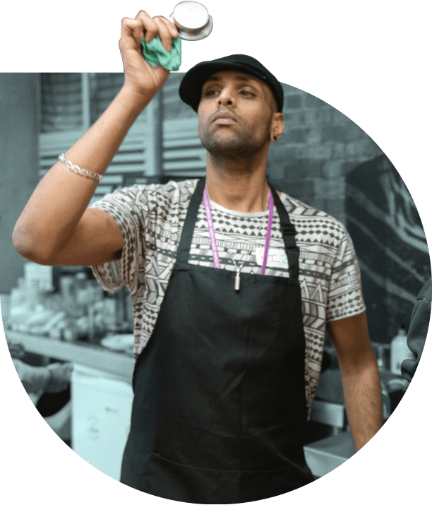 A person with a baby in a sling stands up, knotting and weaving threads in a workshop.