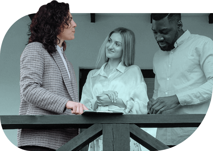 A person with dark curly hair wearing a plaid blazer talks to two colleagues.