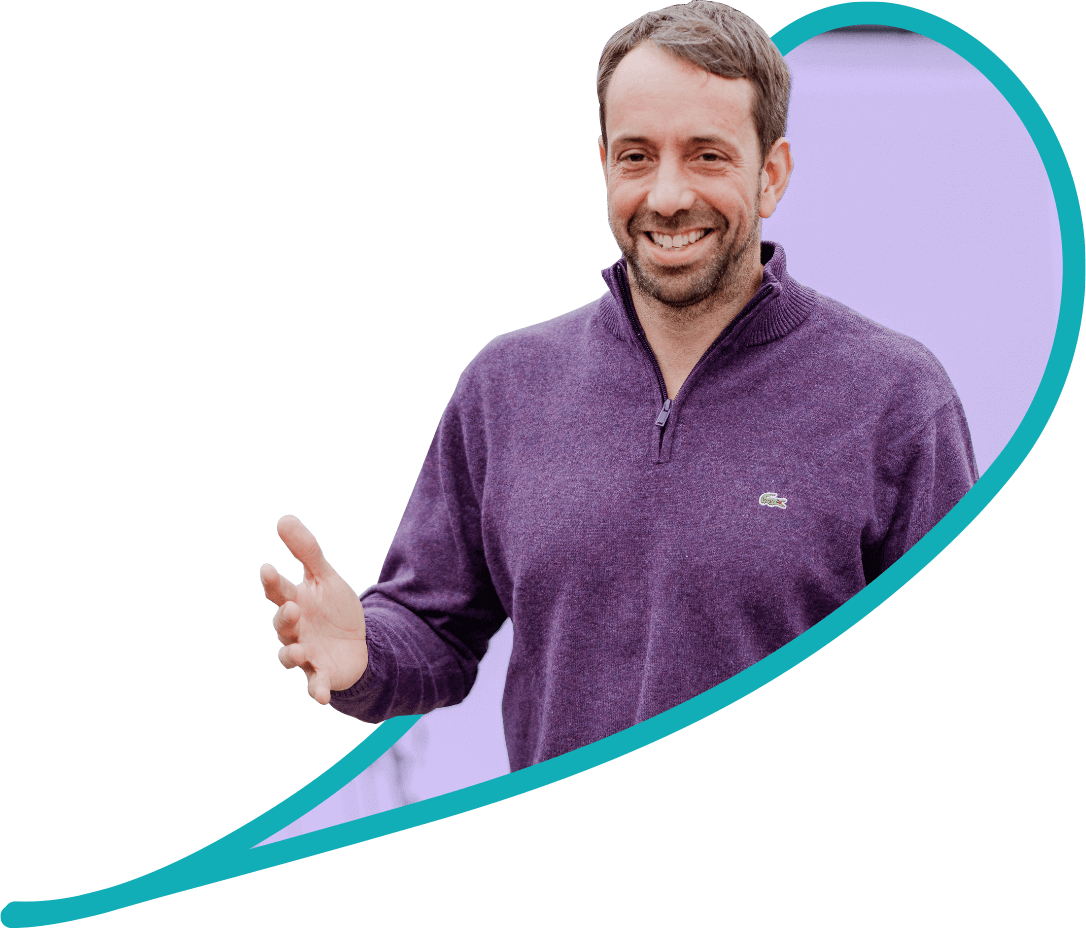 Tom McDonough, Engagement Officer at Camden Disability Action smiles. Tom has brown hair and stubble and is wearing a purple jumper.