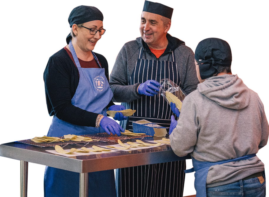 Photo of three bakers smiling, packing flatbreads for Step and Stone social enterprise.